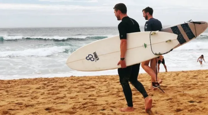 Two surfers carrying boards across a beach